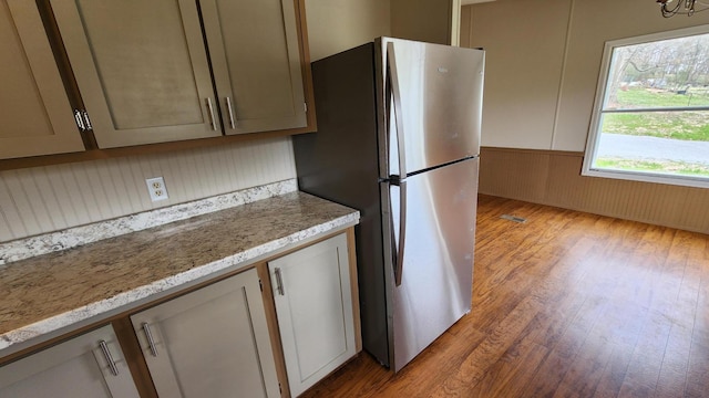 kitchen with freestanding refrigerator, wainscoting, light stone counters, and wood finished floors