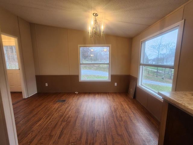 unfurnished dining area with dark wood-type flooring, a chandelier, a textured ceiling, a wainscoted wall, and wooden walls