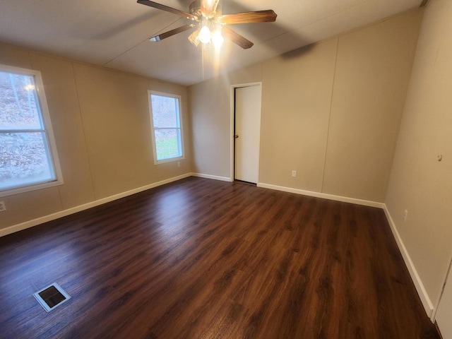 spare room with dark wood-style flooring, ceiling fan, visible vents, and plenty of natural light