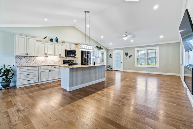 kitchen featuring a center island with sink, stainless steel appliances, hanging light fixtures, and light hardwood / wood-style flooring