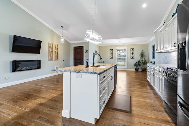 kitchen with pendant lighting, a kitchen island with sink, white cabinets, sink, and hardwood / wood-style flooring