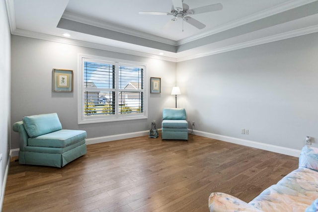 living area featuring hardwood / wood-style flooring, ceiling fan, ornamental molding, and a tray ceiling