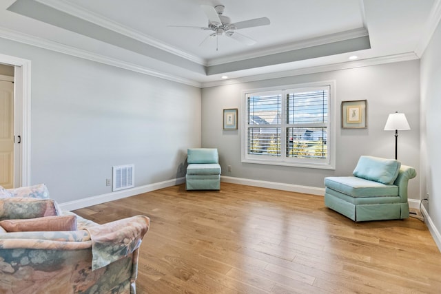 sitting room featuring a tray ceiling, ceiling fan, light wood-type flooring, and ornamental molding