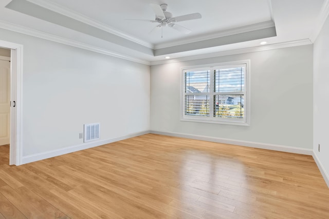 unfurnished room with a raised ceiling, crown molding, and light wood-type flooring