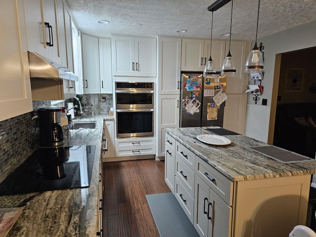 kitchen with dark wood-type flooring, appliances with stainless steel finishes, light stone counters, white cabinets, and decorative light fixtures