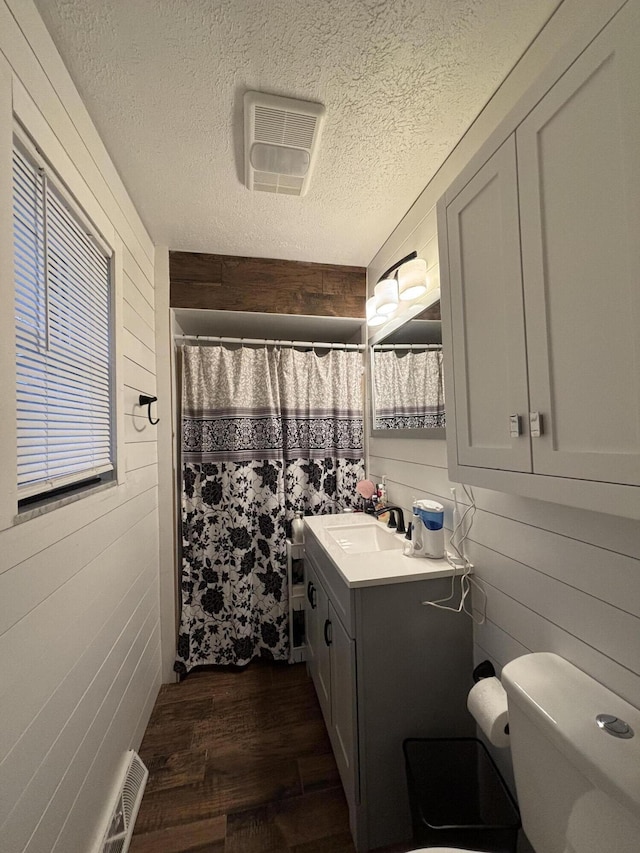 bathroom with vanity, toilet, a textured ceiling, and wood walls