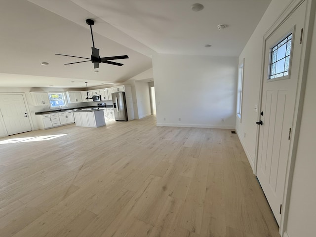 interior space featuring lofted ceiling, ceiling fan, a sink, baseboards, and light wood-style floors