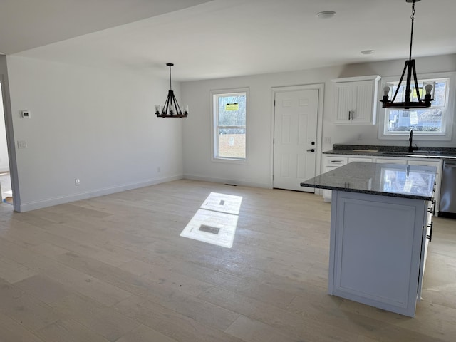 kitchen featuring light wood finished floors, dark stone counters, a center island, white cabinetry, and a sink