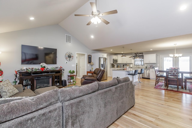 living room featuring ceiling fan with notable chandelier, light wood-type flooring, and high vaulted ceiling