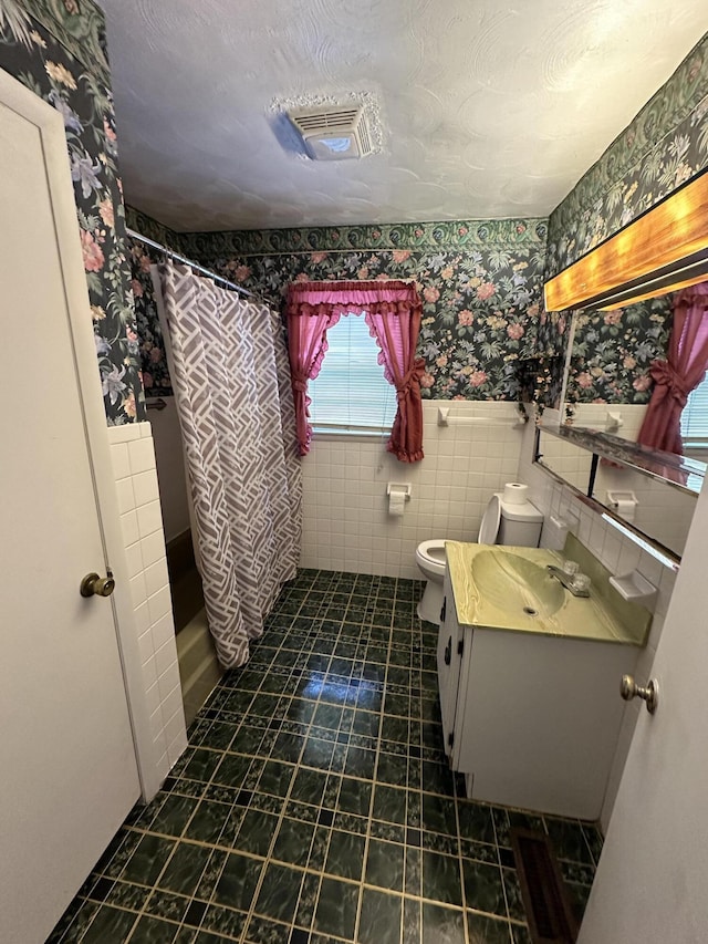 bathroom featuring toilet, vanity, visible vents, wainscoting, and wallpapered walls