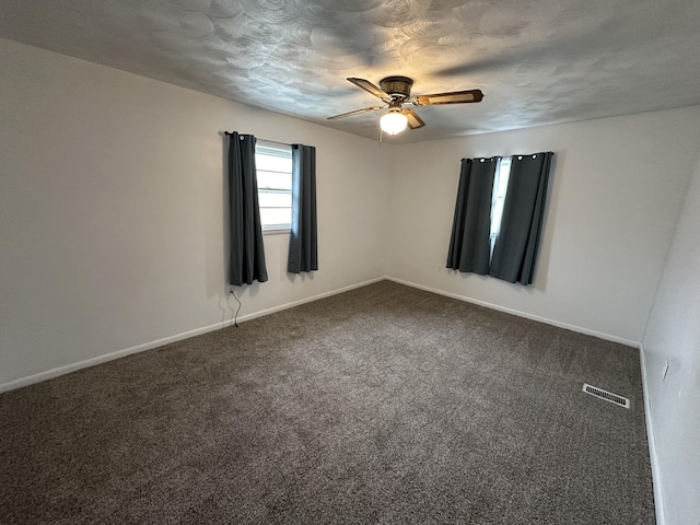 empty room with visible vents, dark carpet, baseboards, and ceiling fan