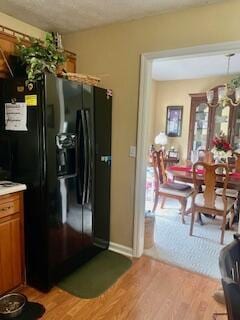 kitchen with black fridge with ice dispenser and light wood-type flooring