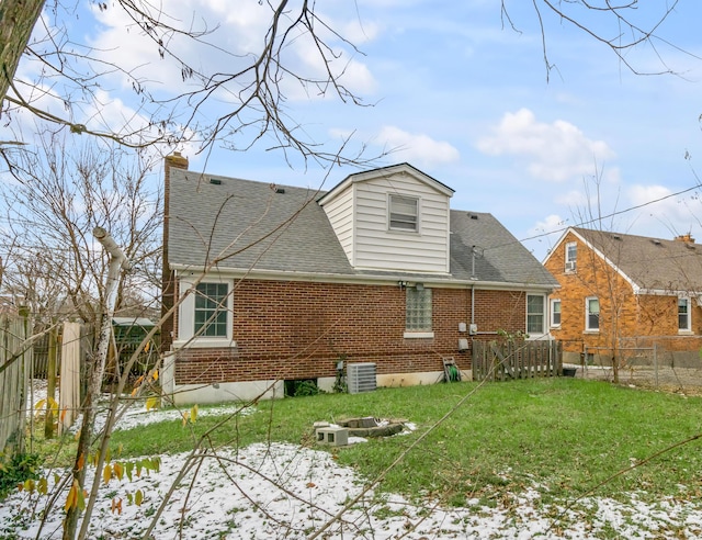 snow covered rear of property with a fire pit, a lawn, and central AC