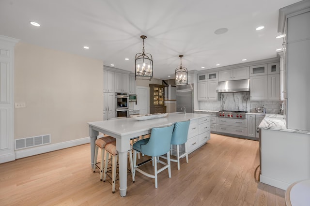1821 Delong Rd, Lexington, KY 40515 - kitchen with appliances with stainless steel finishes, under cabinet range hood, an inviting chandelier, a center island with sink, and gray cabinets
