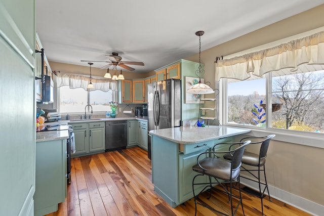 kitchen featuring light wood-type flooring, a sink, decorative light fixtures, stainless steel appliances, and a peninsula