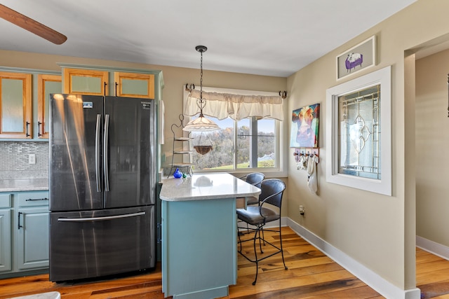 kitchen featuring baseboards, tasteful backsplash, wood finished floors, and freestanding refrigerator