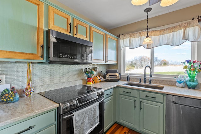 kitchen featuring a sink, appliances with stainless steel finishes, green cabinets, decorative light fixtures, and tasteful backsplash