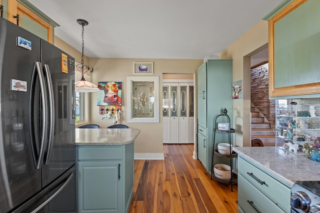 kitchen with baseboards, hardwood / wood-style floors, light stone counters, freestanding refrigerator, and hanging light fixtures