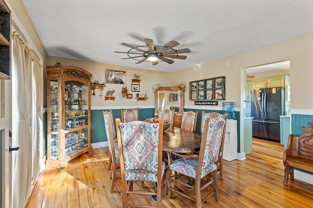 dining area with light wood-style floors, ceiling fan, and wainscoting