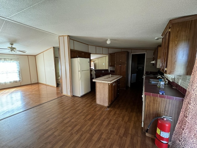 kitchen with sink, dark wood-type flooring, white refrigerator, a textured ceiling, and a kitchen island