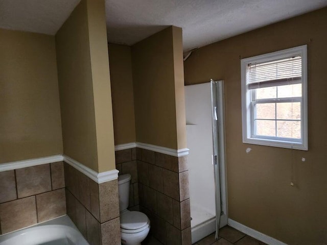 bathroom with a washtub, a textured ceiling, tile walls, tile patterned flooring, and toilet