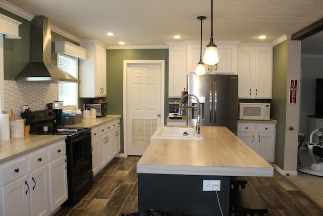 kitchen with black / electric stove, wall chimney exhaust hood, a center island with sink, stainless steel fridge with ice dispenser, and hanging light fixtures