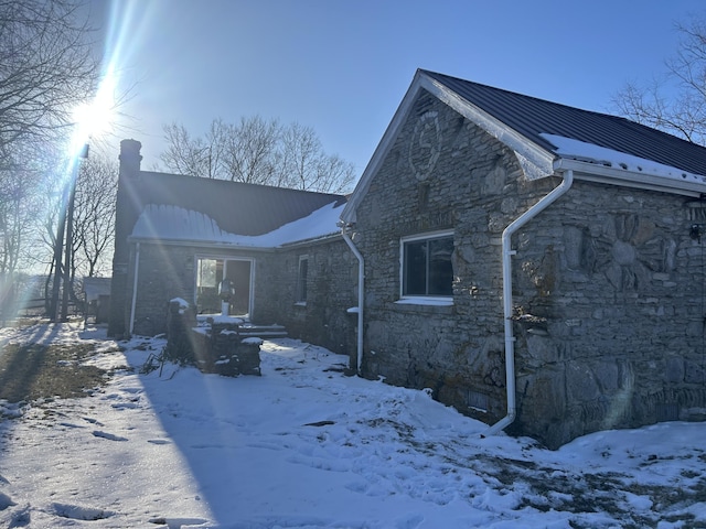 view of snow covered exterior with metal roof, stone siding, and a standing seam roof