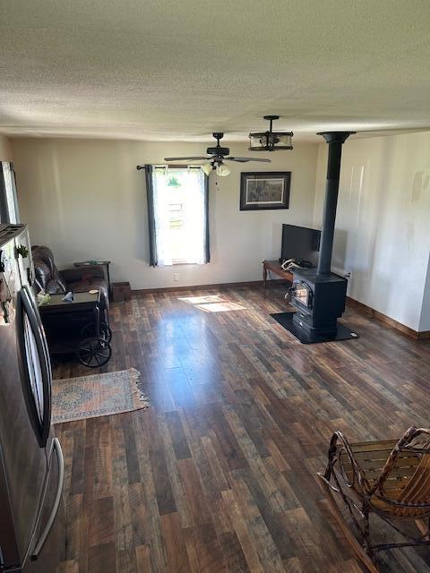 living room with a textured ceiling, dark hardwood / wood-style flooring, a wood stove, and ceiling fan