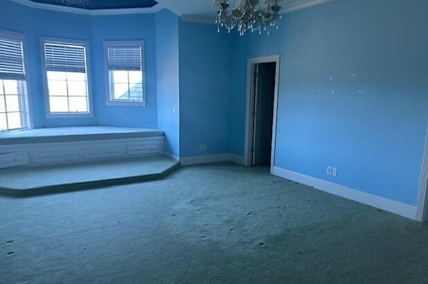 carpeted spare room with crown molding and a notable chandelier