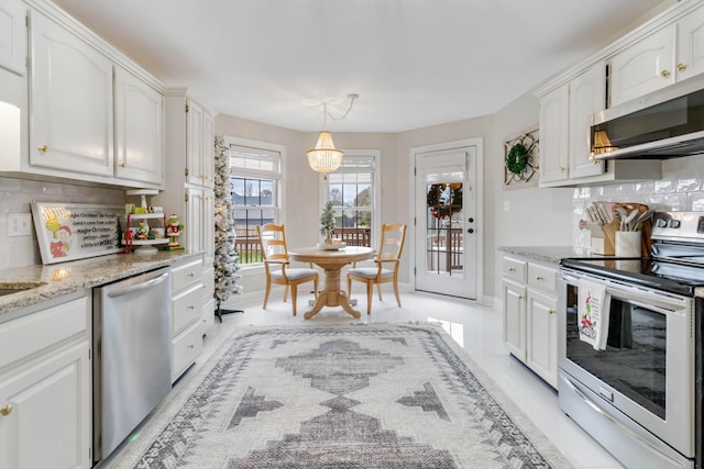 kitchen featuring light stone countertops, appliances with stainless steel finishes, backsplash, white cabinets, and hanging light fixtures