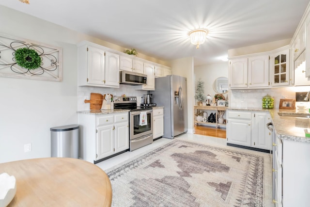 kitchen with tasteful backsplash, light stone counters, stainless steel appliances, sink, and white cabinetry