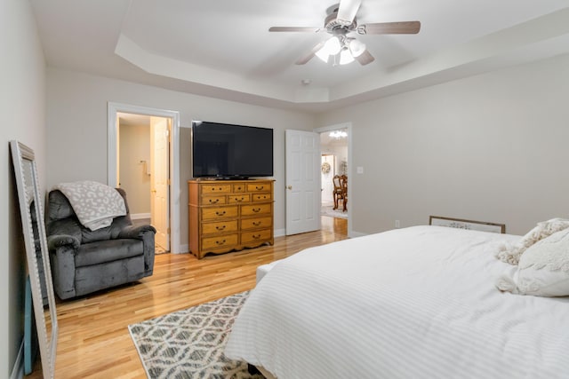 bedroom with hardwood / wood-style flooring, a raised ceiling, and ceiling fan