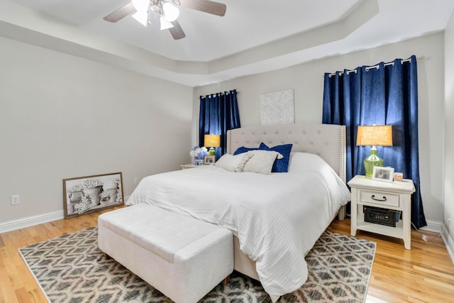 bedroom with hardwood / wood-style floors, a tray ceiling, and ceiling fan