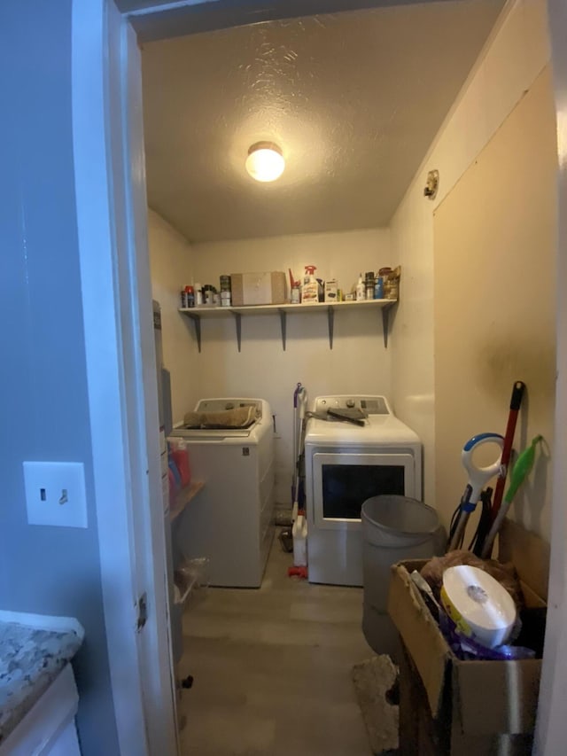 laundry room with washing machine and dryer, a textured ceiling, and light wood-type flooring