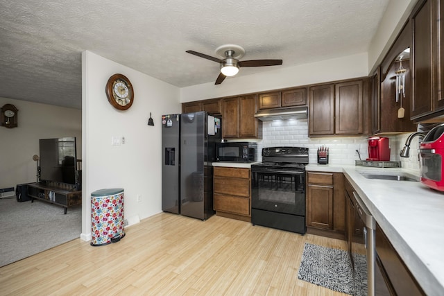 kitchen with under cabinet range hood, a sink, light countertops, backsplash, and black appliances