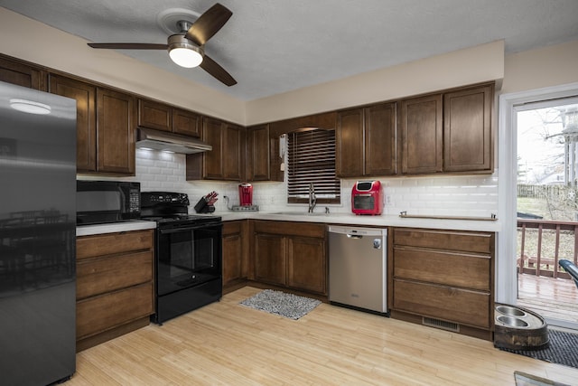 kitchen featuring light wood finished floors, light countertops, a sink, under cabinet range hood, and black appliances