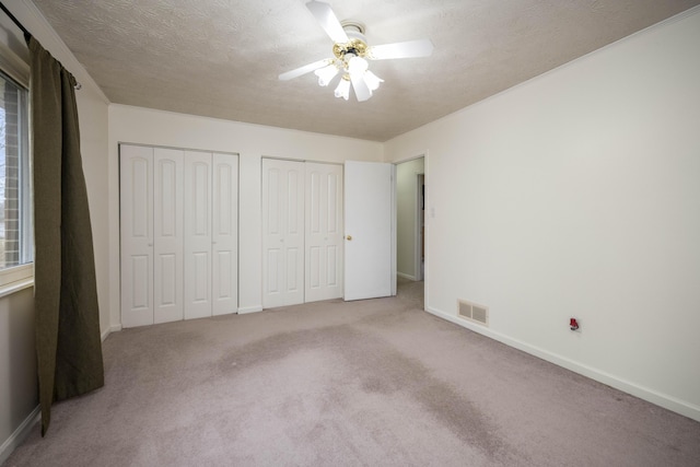 unfurnished bedroom with baseboards, visible vents, a textured ceiling, carpet flooring, and multiple closets