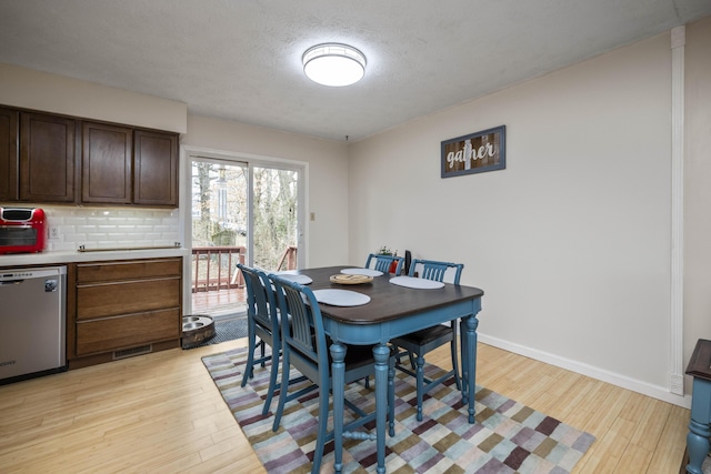 dining space featuring light wood-style flooring, baseboards, and a textured ceiling