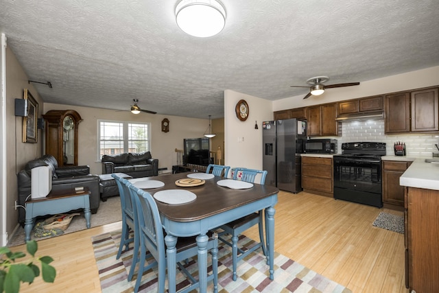 kitchen featuring under cabinet range hood, light countertops, black appliances, light wood finished floors, and tasteful backsplash