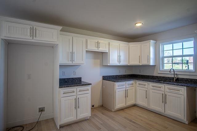 kitchen featuring dark stone countertops, white cabinetry, sink, and light hardwood / wood-style flooring