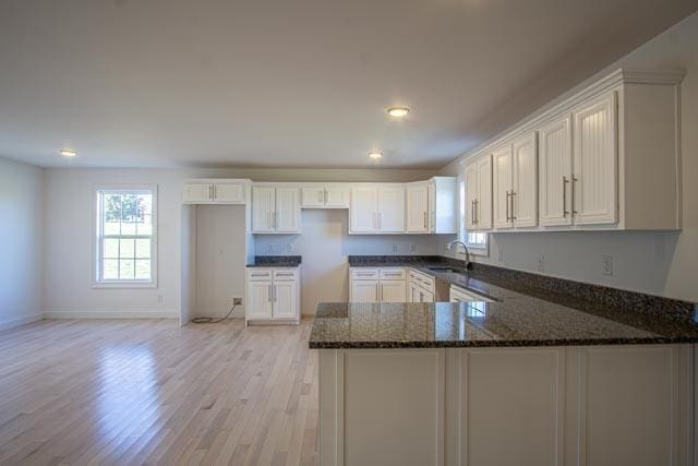 kitchen with white cabinetry, sink, dark stone countertops, kitchen peninsula, and light hardwood / wood-style floors