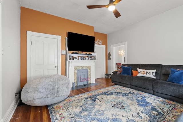 living room featuring dark hardwood / wood-style floors, a stone fireplace, and ceiling fan