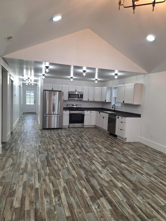 kitchen with appliances with stainless steel finishes, vaulted ceiling, sink, white cabinets, and dark hardwood / wood-style floors