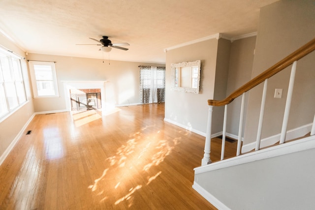 unfurnished living room with ceiling fan, a fireplace, wood-type flooring, and ornamental molding