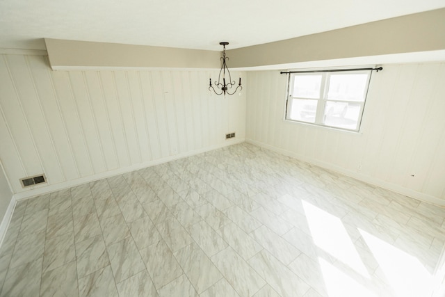 unfurnished room with an inviting chandelier and wooden walls