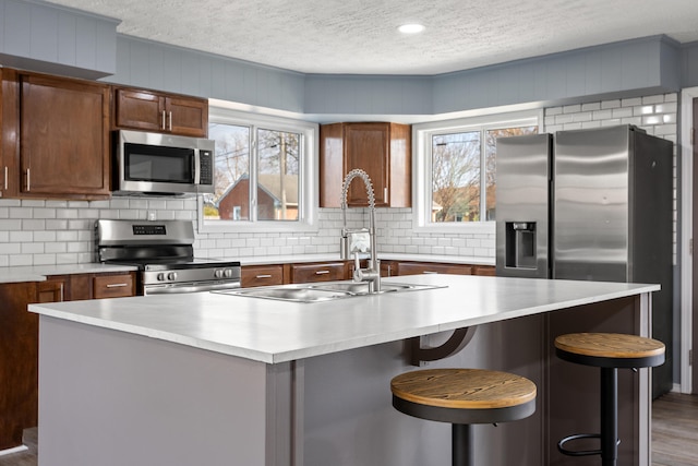 kitchen featuring a wealth of natural light, a center island with sink, wood-type flooring, and appliances with stainless steel finishes