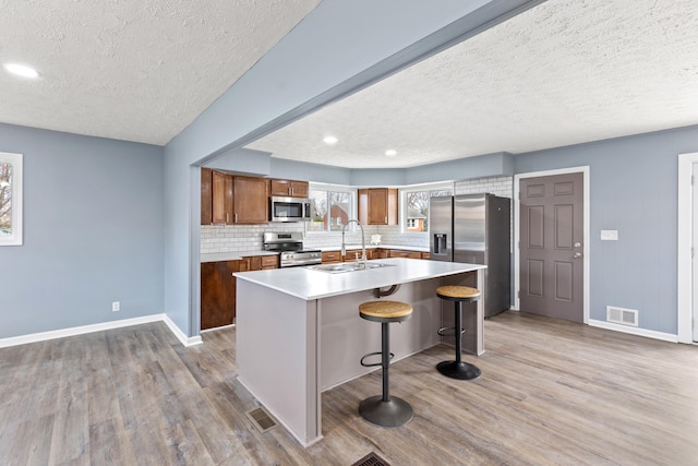 kitchen featuring sink, stainless steel appliances, hardwood / wood-style floors, a textured ceiling, and a center island with sink