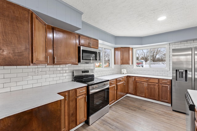 kitchen with appliances with stainless steel finishes, a textured ceiling, tasteful backsplash, and light hardwood / wood-style flooring