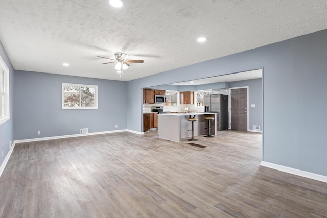 unfurnished living room featuring ceiling fan, light hardwood / wood-style floors, sink, and a textured ceiling