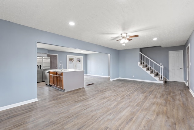 unfurnished living room with ceiling fan, sink, light wood-type flooring, and a textured ceiling